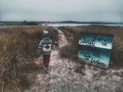 Photo of a child heading down a beach path with a dog.